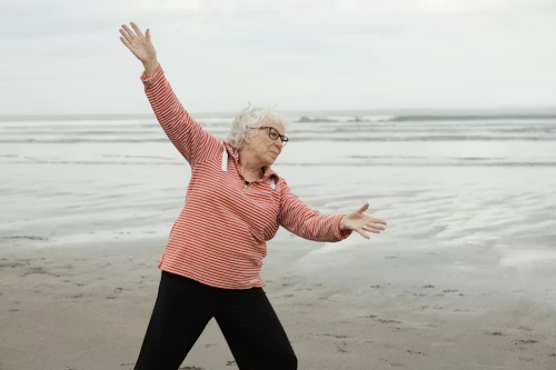 Elderly woman doing yoga poses along the beach